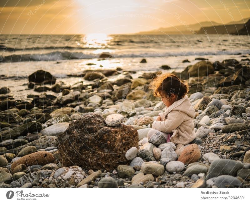 Girl sitting on rocky beach Playing Stone Sit Beach Toddler Interest Cute Infancy seaside Intellect Creativity Serene Coast Vacation & Travel Action Child