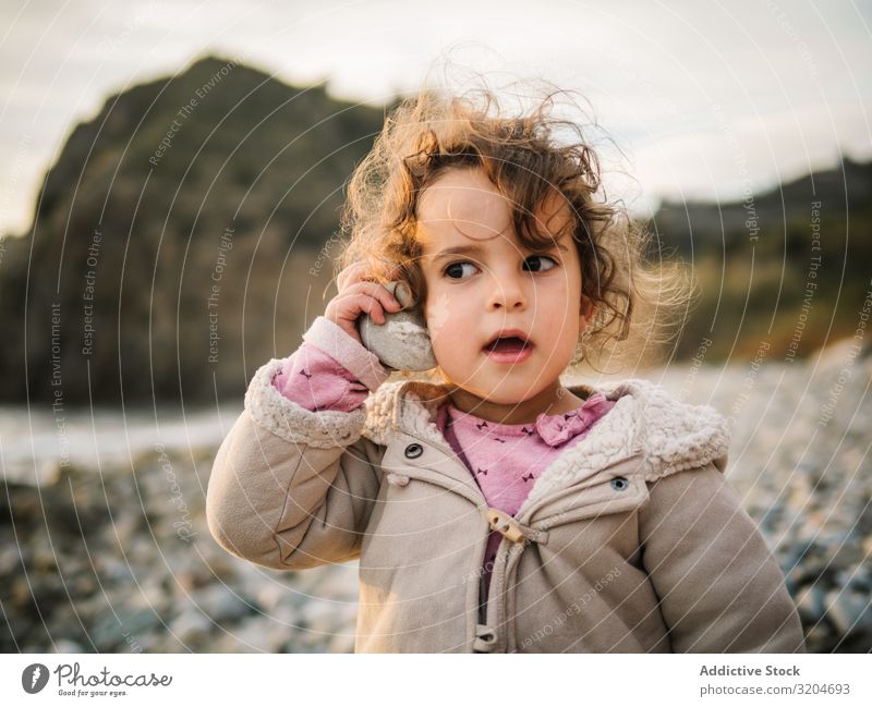 Toddler girl playing with seashell on beach Girl Playing Beach Child attention rapt Portrait photograph Listening conch Resting Nature Interest Discovery