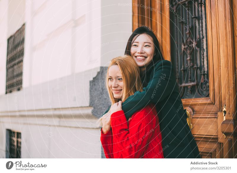 Cheerful female friends hugging near ornamental door Friendship Embrace Smiling Looking away Door Street Building City Mixed race ethnicity Together Woman