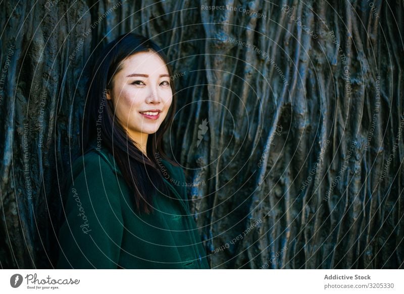 Cheerful Asian woman leaning on rough wall Woman Wall (building) Lean Smiling Looking away Root Tree Street City asian Ethnic Rough Relief Surface Lifestyle