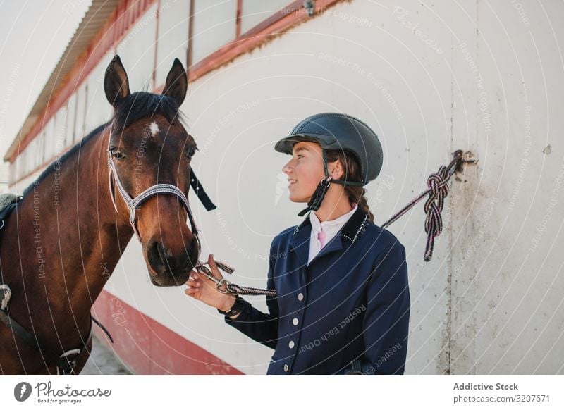 Woman in jockey outfit standing with horse woman stroke animal equestrian teen young pet friend love caress helmet touch beautiful mammal relationship stable