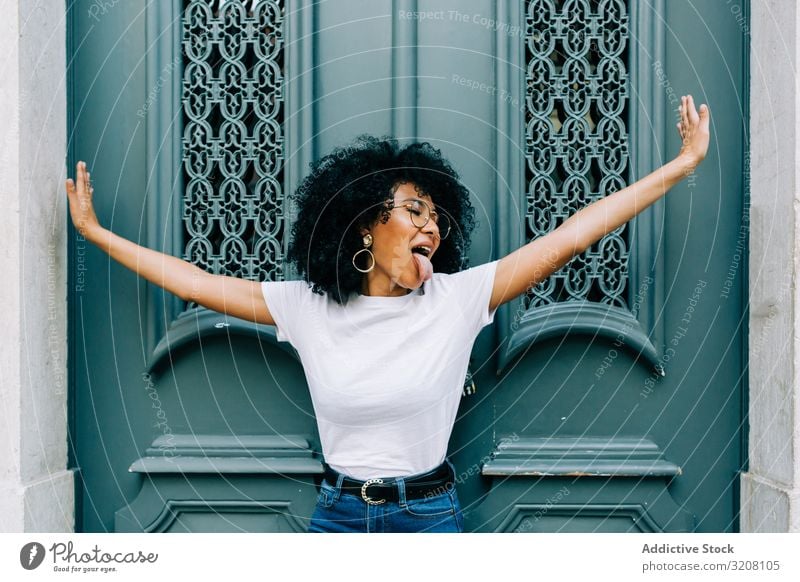 Stylish ethnic female with outstretched arms woman door tongue sticking playful stylish trendy hairstyle young african american person casual attractive