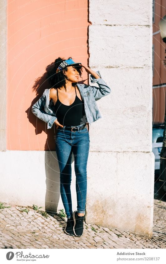 Pretty ethnic female leaning on wall and holding head woman fashion stylish trendy clothing glamorous outfit headband jeans denim young african american casual