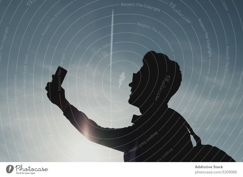 Silhouette of man with phone against sky selfie millennial smartphone silhouette technology mobile male modenr sunlight bright carefree lifestyle leisure fun