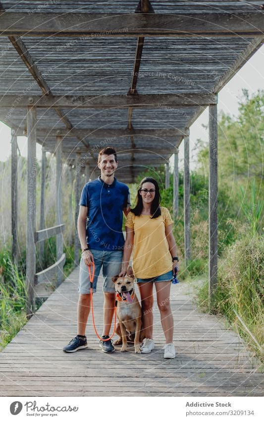 Happy adult couple standing with dog at countryside play happy casual cheerful leash brown rural wooden woman tree terrace greenery daylight pet together