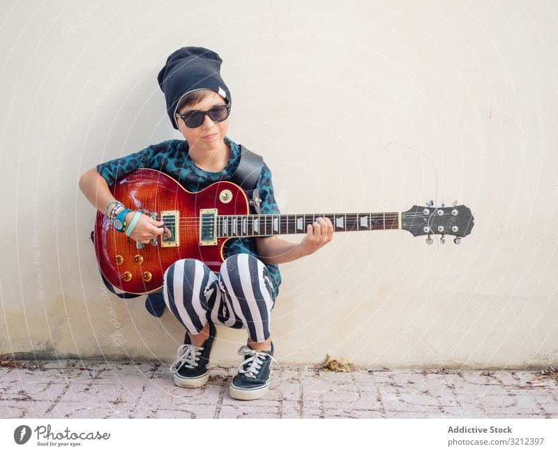 Energetic kid holding guitar boy playing rockstar colorful childhood fashion sign gesture artist musician festive laugh little contemporary funny having fun
