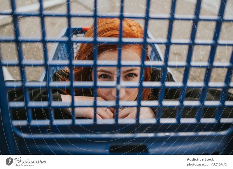 Woman looking through trolley grate in shopping cart woman attractive young beautiful casual cheerful smiling smart modern joy redhead female pretty pleasure