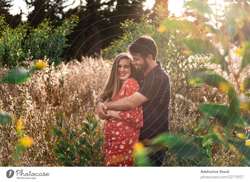 Young happy couple embracing in beautiful garden pregnant man woman hugging tenderness park expecting love relationship together lover husband wife boyfriend