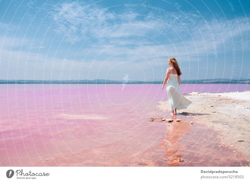 Back view of cute teenager woman wearing white dress walking on a amazing pink lake young saline romantic tourism summer happy alone sea colorful nature water