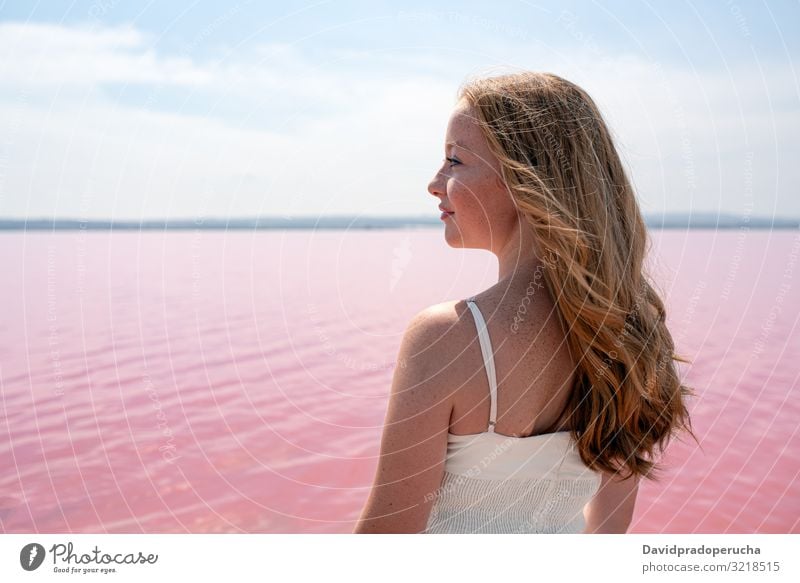 Side view of cute teenager woman wearing summer clothes standing on an amazing pink lake young romantic white freckles happy alone sea colorful adolescent water