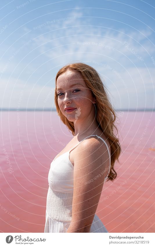 Side view of cute teenager woman wearing summer clothes standing on an amazing pink lake young romantic white freckles happy alone sea colorful adolescent water
