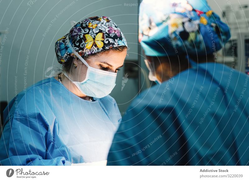Concentrated female surgeon at work woman doctor surgery hospital operation medicine profession concentration young serious attentive surgical gown blue cap