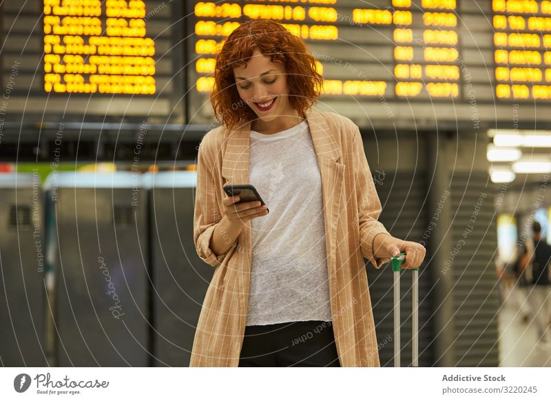 Red haired young woman using smartphone at station travel business vacation smile tourist railway departure suitcase passenger female terminal waiting schedule