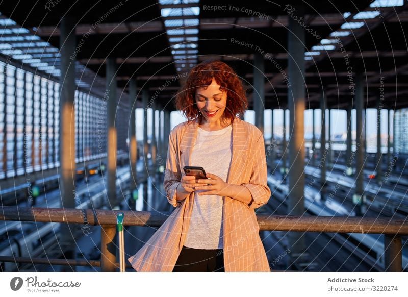 Smiling young woman browsing phone at station railway smartphone call smile travel business vacation tourist communication terminal departure female suitcase