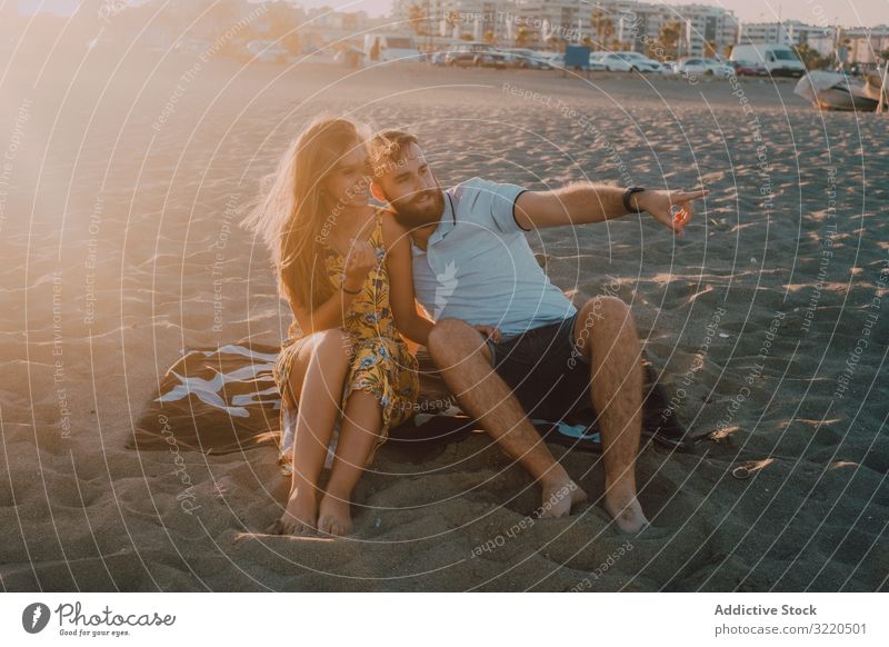 Tender couple talking and pointing in sunlight on towel beach romantic love happy embracing tender hugging anniversary together dating lovely relationship