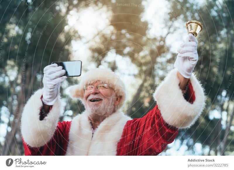 Happy Santa Claus with smartphone and bell santa selfie holiday man christmas event using celebration senior male cheerful joyful bearded gray-haired