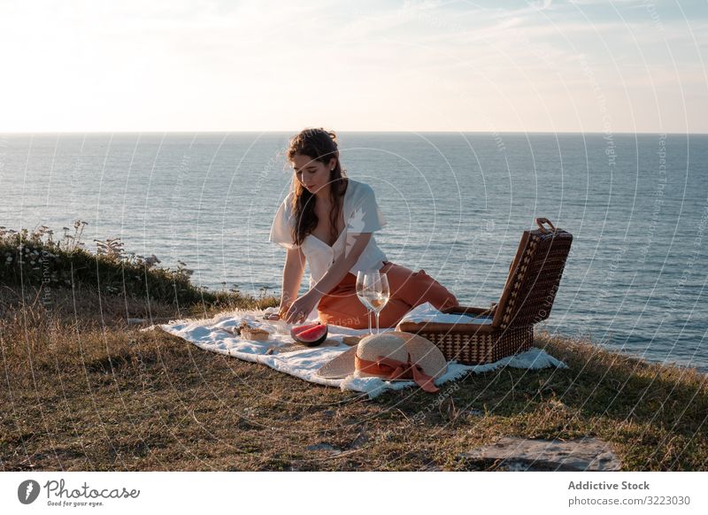Woman with glass of drink on picnic mat near sea and mountains woman seaside beach summer reading leisure sky relax vacation summertime vintage fashion