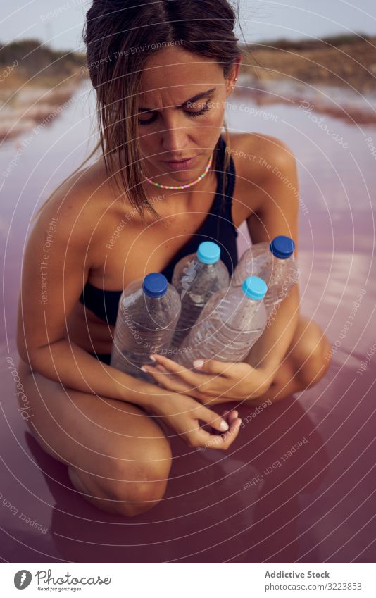 Concerned female in swimsuit collecting trash in natural lake pollution water contamination woman concerned pool pick bottle plastic red lagoon planet safety