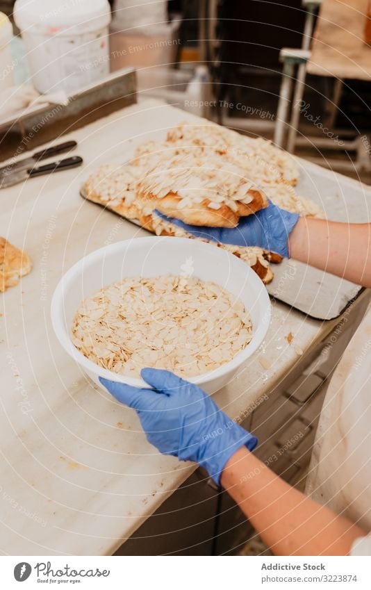 Crop baker making buns with almond flakes confectioner cook kitchen bakery fresh bowl counter process treat nut ingredient preparation professional work job