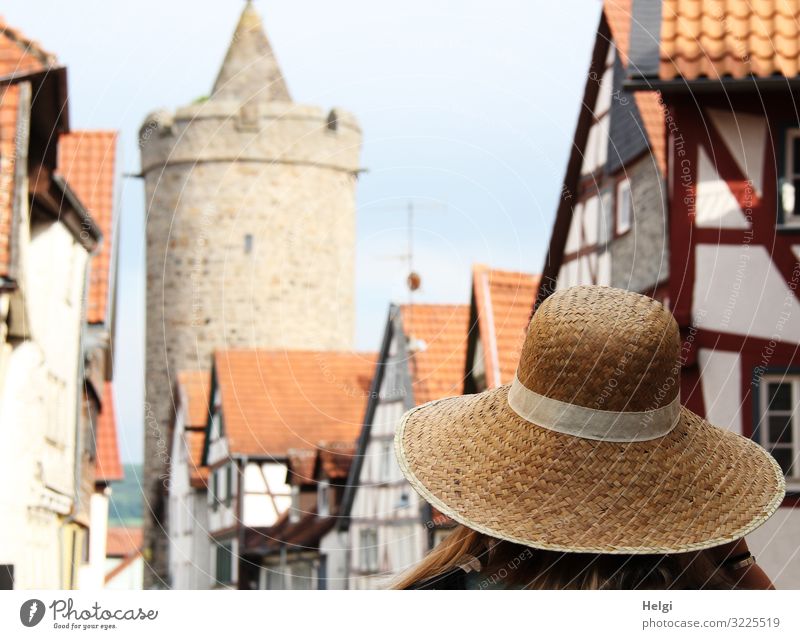 Lady with sun hat walks in an old town with half-timbered houses and historical tower Human being Adults 1 as field Town Old town House (Residential Structure)