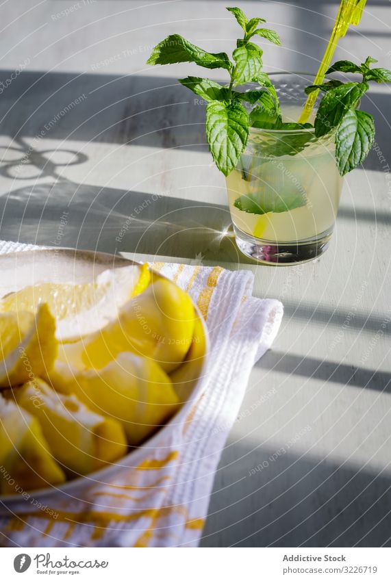 Glass of fresh lemonade next to plate with cut lemons on table glass piece juice kitchen wooden rustic homemade mint fruit drink food healthy natural citrus