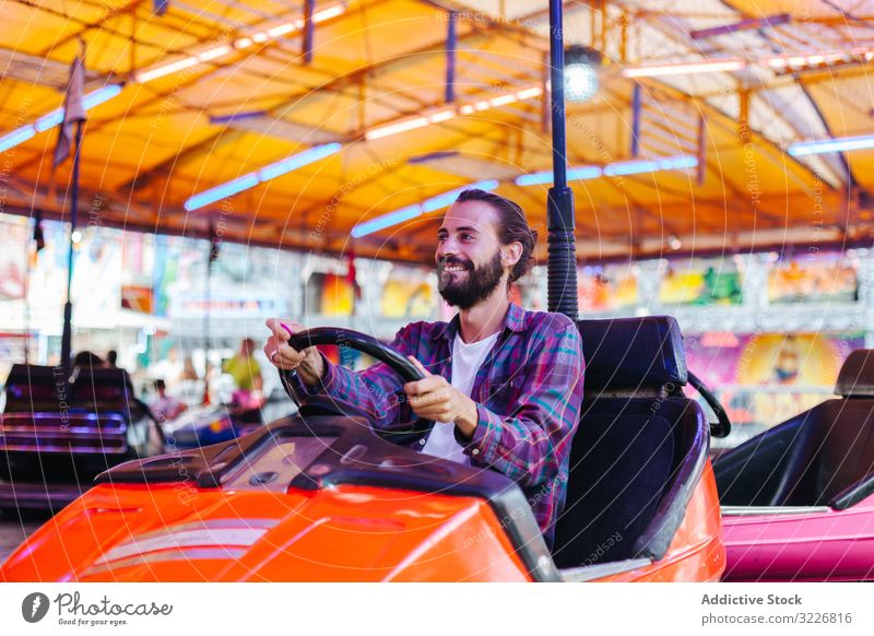 Happy hipster man riding electric car in amusement park ride joyful happy casual smile having fun attraction carnival fairground vibrant entertainment young