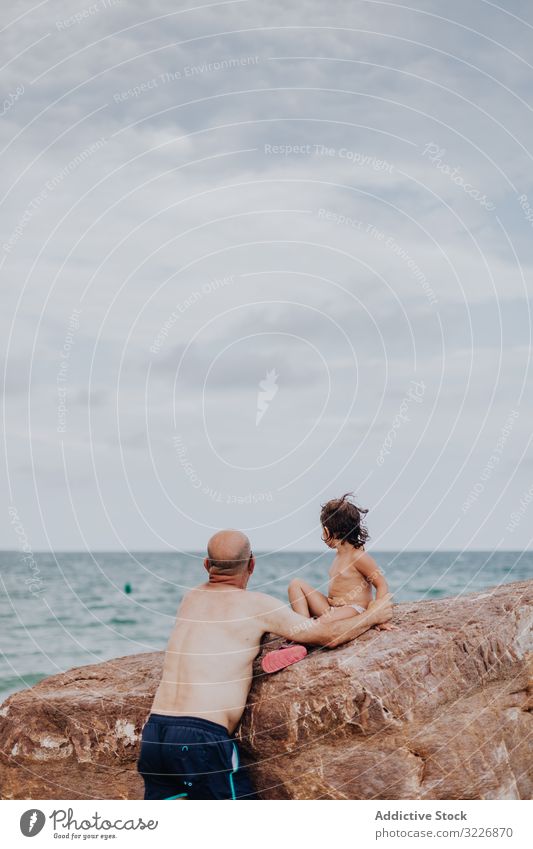 Old man holding small girl on stony beach grandfather granddaughter caring ocean vacation family tender embracing elderly child water granddad nature shore