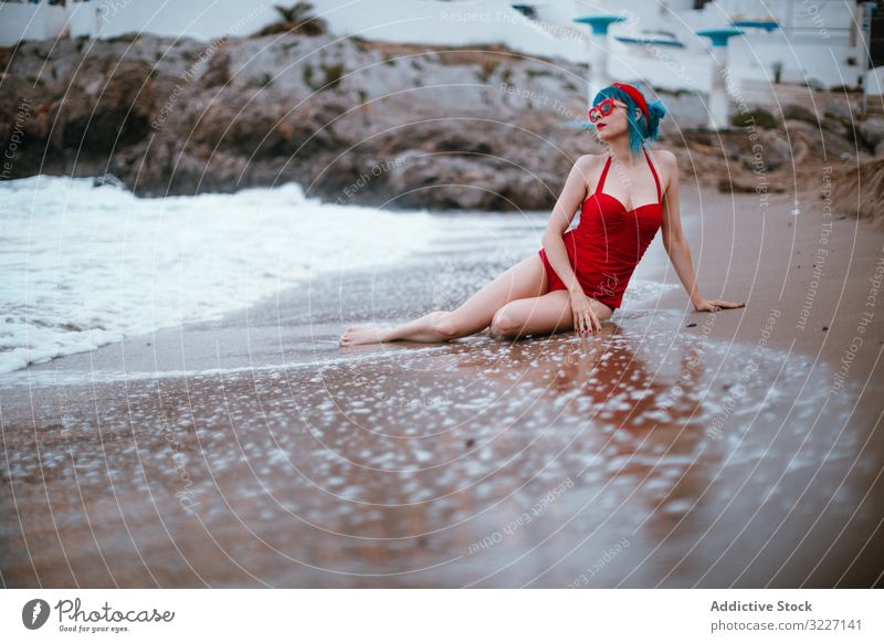 Relaxed woman in bright stylish swimsuit sitting on sandy beach sea retro adult sensual relaxation fashion vintage elegant enjoyment swimwear classic lady