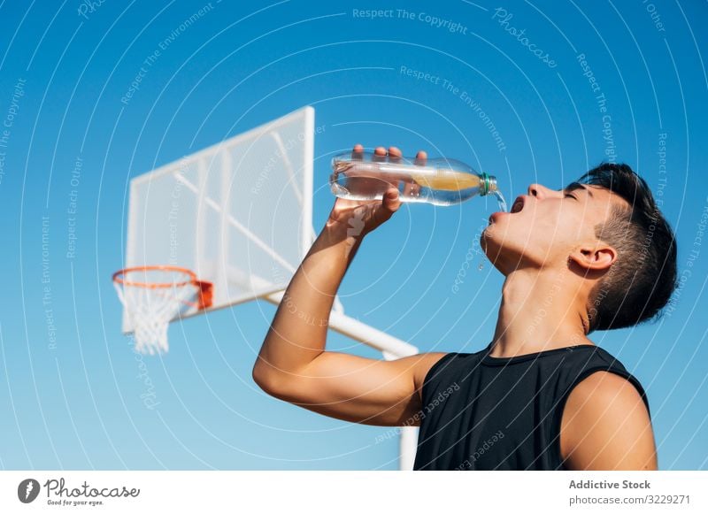 Young man playing on basketball court outdoor drinking water athlete competition sports equipment adult recreation action portrait active activity asphalt