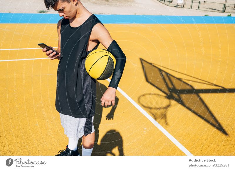 Male basketball player using his smartphone resting after training people outdoors man city sport street urban young activity yellow city life court daylight