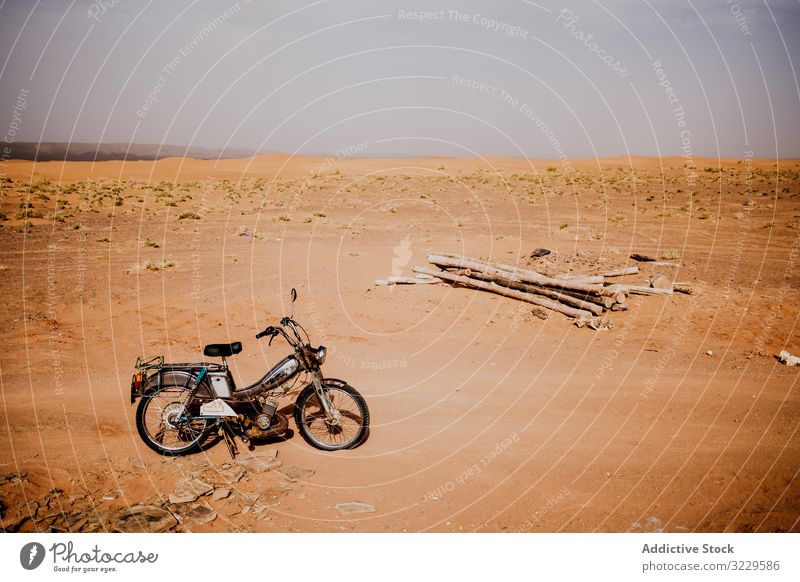 Motorbike and logs in desert motorcycle travel sand wood pile morocco africa parked transport vehicle motorbike trip journey lumber arid dry drought sky nature
