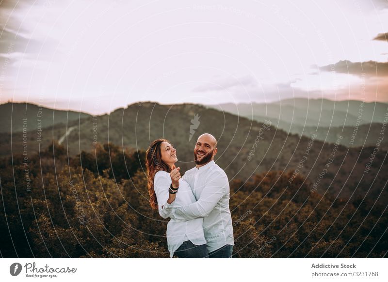Affectionate couple having fun on hilly valley affectionate field nature happy mountain love smile hills countryside white shirt grass young adult together