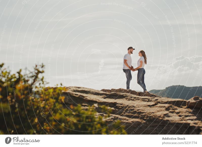 Loving couple holding hands while standing at mountain cliff love travel romantic hugging summer hilly slope cheerful modern casual matching identical young