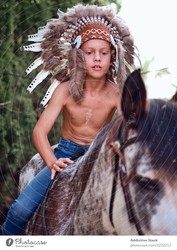 Concentrated child saddling stallion boy horse ride authentic saddle war bonnet indian costume training concentrated native art serious headdress head wear hat