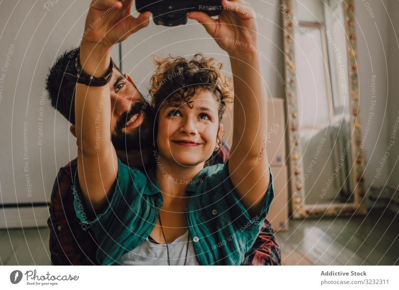 Joyful couple embracing and taking selfie on camera at home hipster joyful affection hugging using photo sit rest floor apartment cuddling house domestic smile