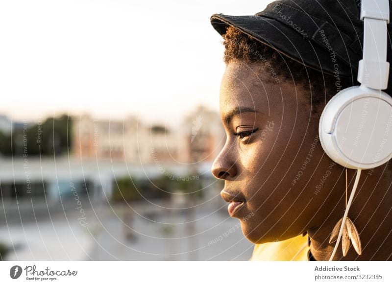 Peaceful female enjoying music and relaxing on balcony woman headphones peaceful content trendy african american lean glass jacket listen happy sound young