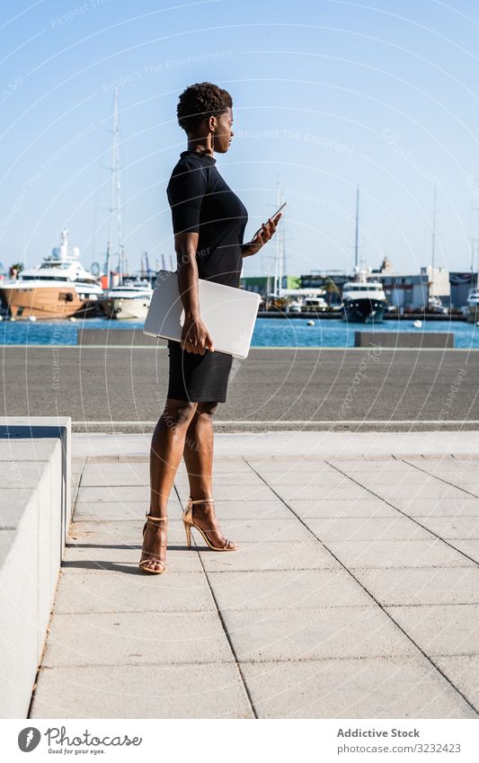 Black woman using mobile phone on the street laptop relax surfing african american female modern elegant dress black building pavement online businesswoman