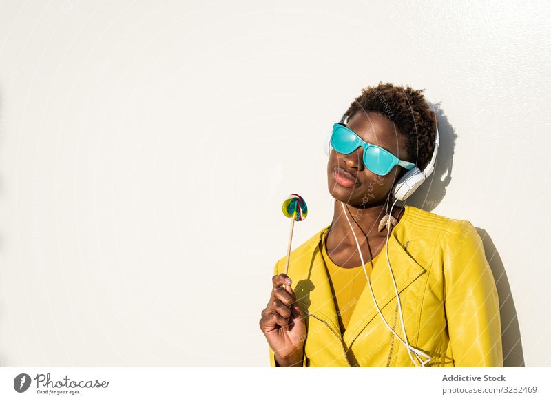 Black woman eating candy lollipop cool trendy african american female jacket yellow sunglasses enjoy sweet summer fun stick young fashion cute relax chill