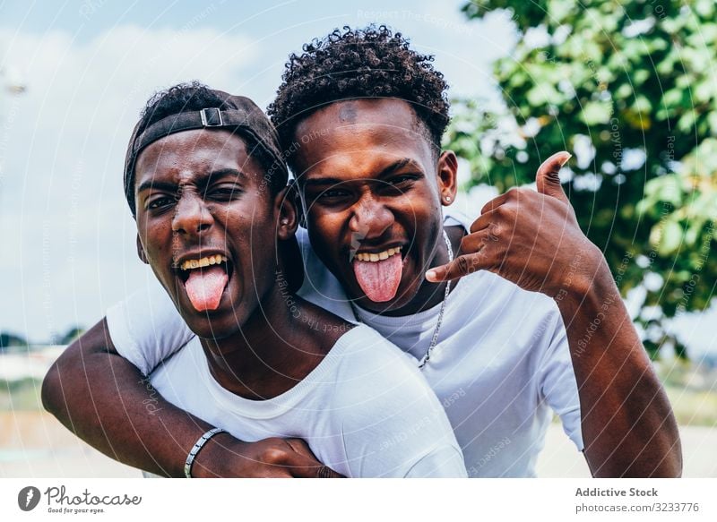 Smiling black friend hugging and grimacing gesturing with hands men showing tongue confident grimace friendship african american funny face crazy happy gesture
