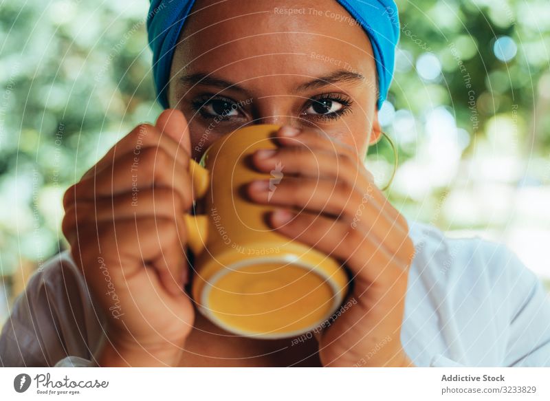 Woman in turban drinking coffee woman rest patio pleased smile content enjoy gaze tree head wrap rural costa rica greenery happy young terrace cup relax