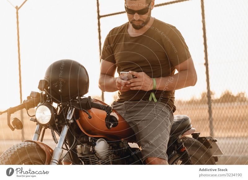Man sitting on motorcycle and surfing mobile man smartphone rest using sunglasses focused wistful male field transport road bike biker break device gadget