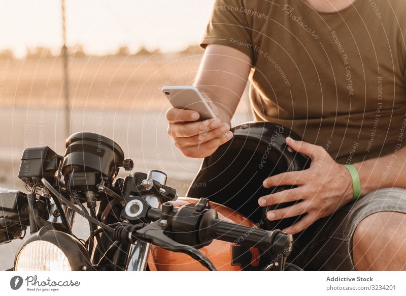 Man sitting on motorcycle and surfing mobile man smartphone rest using sunglasses focused wistful male field transport road bike biker device gadget watching