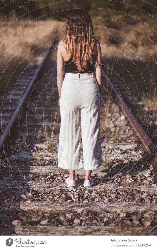 Long haired woman standing on railways overgrown with dry grass road travel nostalgia journey track railroad female classic passenger tourism destination
