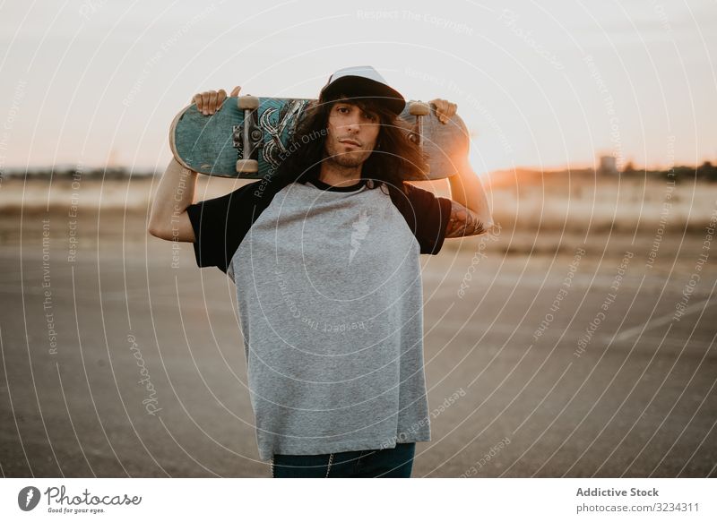 Cool confident teenager with skateboard looking at camera hipster cool man style millennial rural country street style cap generation sunset modern trendy