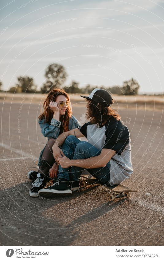 Skaters sitting on empty rural road chatting in sunlight couple teen skater together generation sport countryside hipster asphalt in love fun active modern