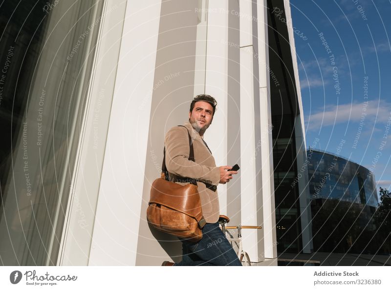 Businessman with smartphone leaning on building on city street businessman wall downtown male professional entrepreneur device gadget using browsing success job