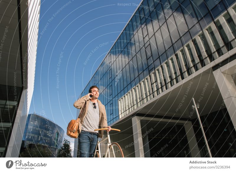 Man phoning while standing against modern building in downtown smartphone man mobile phone street skyscraper urban talk bike pensive delivery share conversation