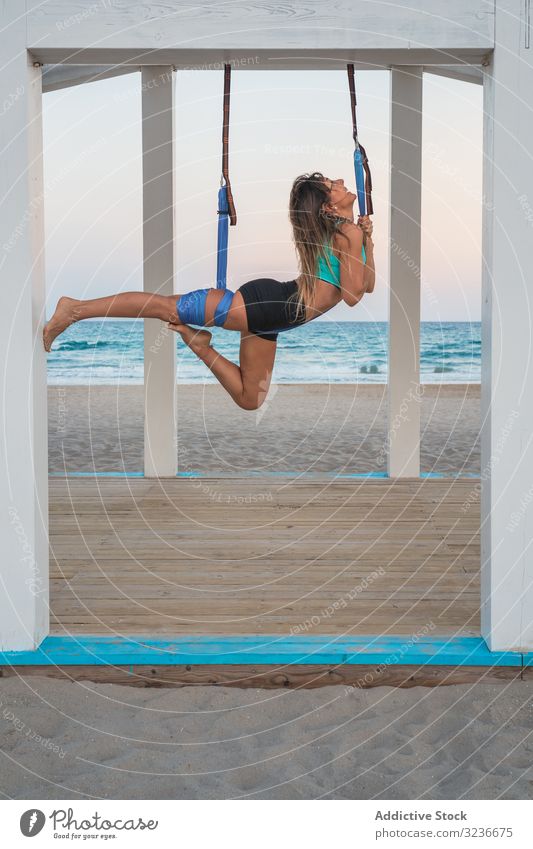 Cheerful woman stretching leg on blue hammock for aerial yoga on wooden stage exercise balance acrobatic fitness anti-gravity yoga young posture training sport