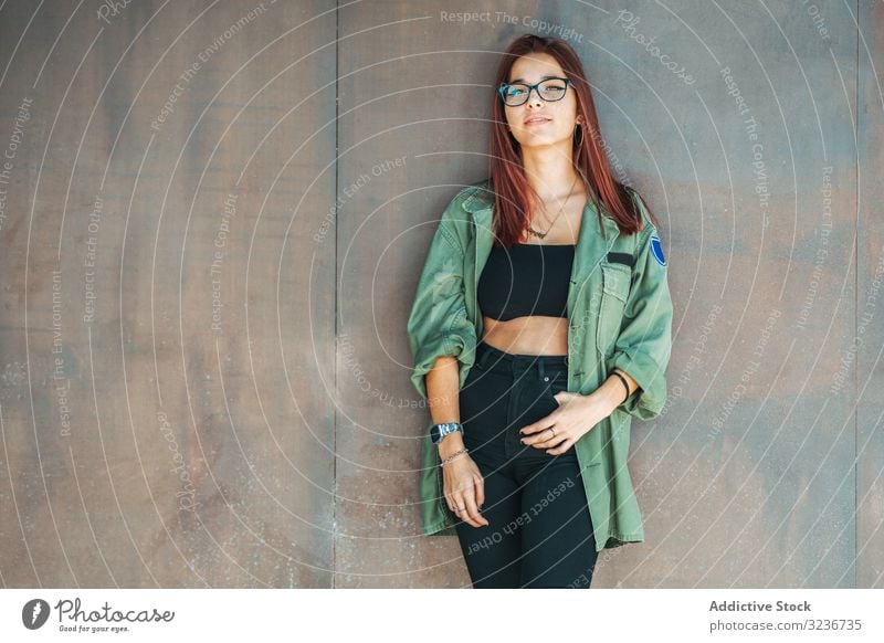 Stylish confident bright woman in glasses leaning on wall and looking at camera stylish smart provocative hairstyle clever attractive female cute beauty pretty