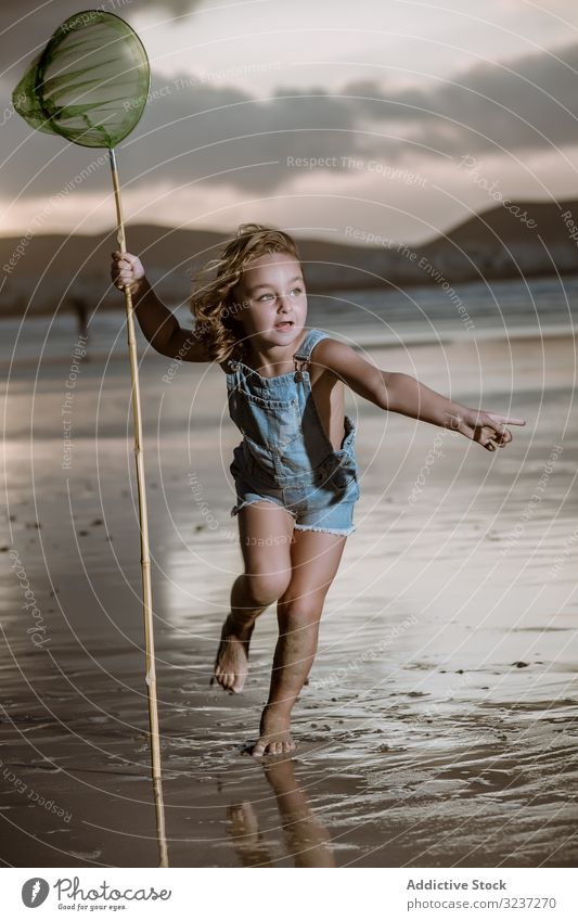Curios kid with butterfly net walking barefoot on wet shore seaside cute childhood nature catch activity little natural coast beach vacation holiday resort sand